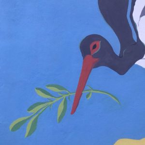 Dipinto murale - cicogna nera che sta planando su un prato, nel becco porta un rametto di ulivo. Moticvi decorativi floreali, fico d'india, finocchietto, lentisco