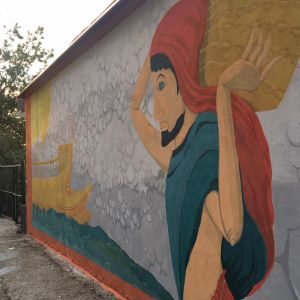 Dipinto murale - antico greco raccoglitore di sale con cappuccio rosso e drappo azzurro, porta il cesto sul mercantile color ocra che si trova sullo sfondo del disegno galleggiando sul mare