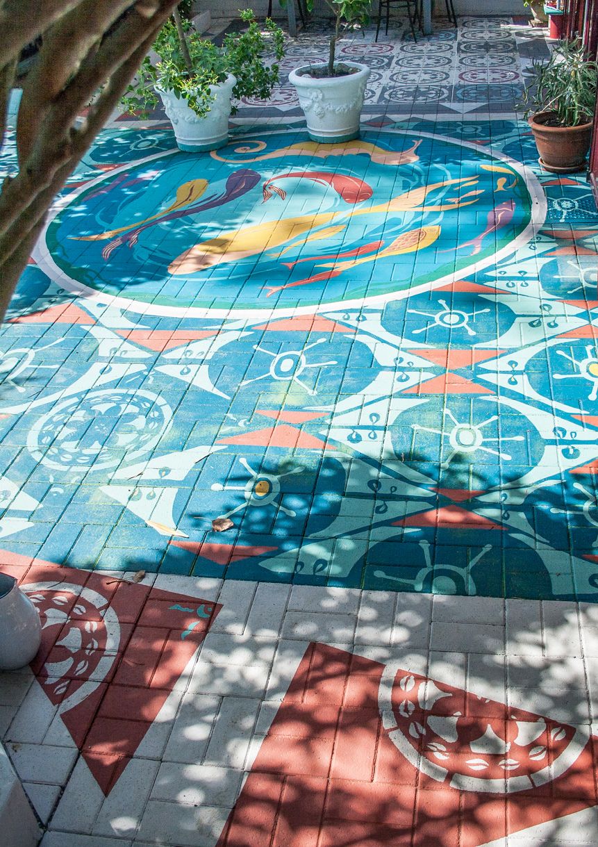 Pavimentazione esterna decorata con motivi floreali blu e arancione e pesci gialli rossi e viola stilizzati eseguiti a pennello e stencil