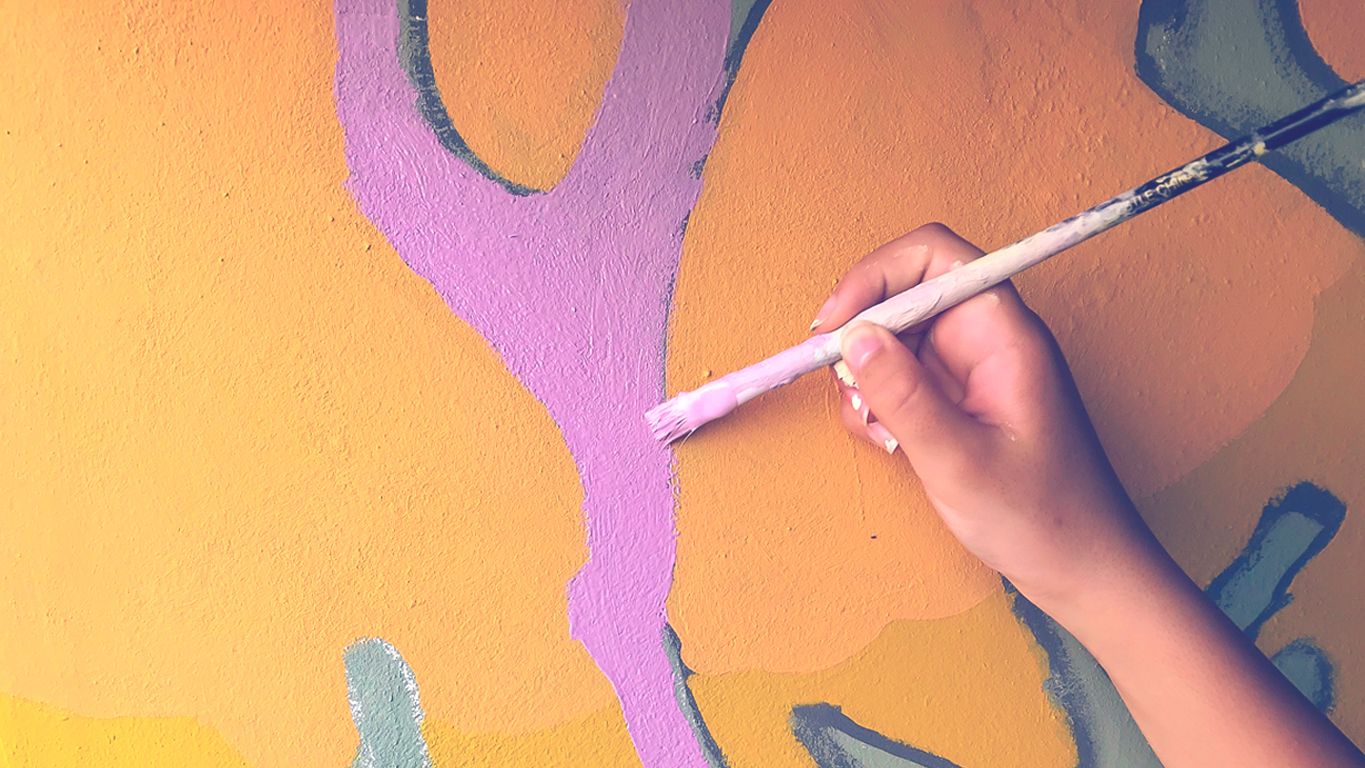 Murale collettivo, mano che dipinge sul  muro, giallo e viola
